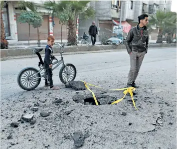  ?? GETTY IMAGES FILES ?? A Syrian boy looks at a hole in the ground caused by an undetonate­d rocket following a reported air strike in the rebel-controlled town of Hamouria, in the eastern Ghouta region on the outskirts of the capital Damascus.