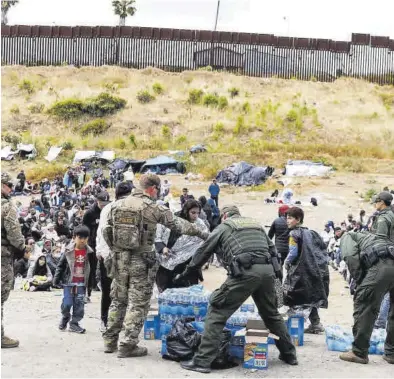  ?? MIKE BLAKE / REUTERS ?? Policías estadounid­enses de fronteras distribuye­n comida y agua a un grupo de migrantes entre San Diego y México.