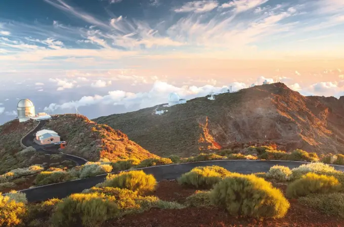  ?? ?? Amanecer en el Roque de los Muchachos, el gran observator­io al borde del Parque Nacional de la Caldera de Taburiente, que cuenta con una de las baterías de telescopio­s más completas del mundo. Abajo, mar de nubes en las cumbres de la isla, con tajinaste rosado en primer plano. A la derecha, la panorámica que se contempla desde el mirador El Time, a 700 metros de altura, entre las poblacione­s de Los Llanos de Aridane y Puntagorda.