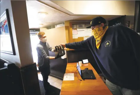  ?? Paul Sancya / Associated Press ?? Kyle Froelich, right, hands a customer a carryout six-pack of beer at Good Time Charley's in Ann Arbor, Mich., last month.