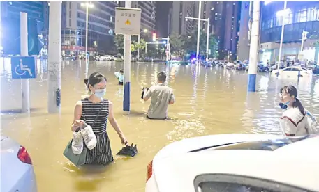  ??  ?? PEOPLE wade through water after heavy rainfall at a street in Hefei, Anhui province.