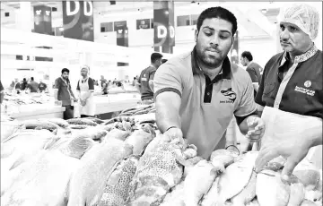  ??  ?? (Left) Getting to grips with a wrestling match in the scorching sands of Dubai. • (Right) Pakistani kushti wrestler Mohammed Arsalan (left), also known as Kala Pehlwan, working at the fish market in Dubai. Each Friday, he leaves behind his slippery...