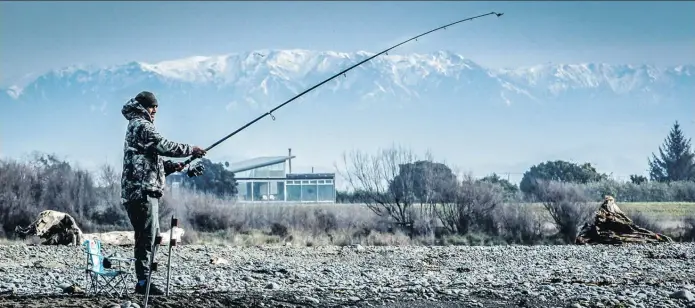  ?? Photo / Hawke's Bay Today ?? A fisherman tries his luck at the Tukituki river mouth at Haumoana, near Hastings, with the snow-capped Kaweka range on the horizon.