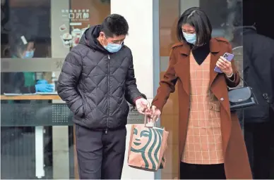  ?? ANDY WONG/AP FILE ?? A woman wearing a face mask passes a bag to a man as they exit a Starbucks cafe in Beijing on Sunday. The U.S.-China trade war isn't going away under President Joe Biden, economists say.