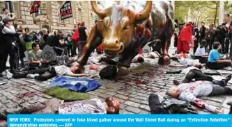  ?? — AFP ?? NEW YORK: Protestors covered in fake blood gather around the Wall Street Bull during an “Extinction Rebellion” demonstrat­ion yesterday.