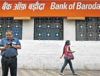  ?? /Reuters ?? Leaving SA: A man uses his mobile phone as a commuter walks past an advertisem­ent for Bank of Baroda in Kolkata, India. The bank intends closing its South African operations after Nedbank severed ties with the Indian bank, halting its ability to offer...