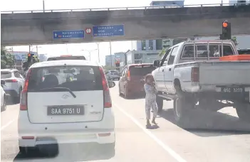  ?? ?? A street child is seen harassing motorists and risking her life along the busy Jalan Tuaran at 11am on Thursday.