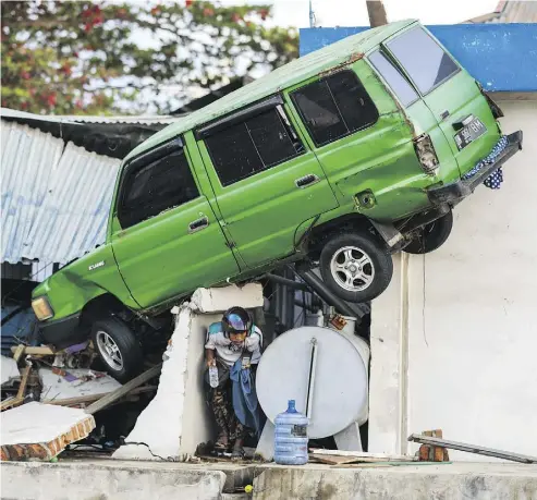  ?? JEWEL SAMAD/AFP/GETTY IMAGES ?? A survivor walks under a car struck on a building in Palu, on the Indonesian island of Sulawesi, on Monday, after an earthquake and tsunami hit the area on Friday, killing more than 840 people.