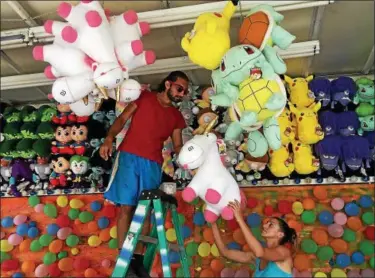  ?? TANIA BARRICKLO — DAILY FREEMAN ?? April Naimon, right, hands a stuffed unicorn to Josh Ristick on Monday as they prepare a balloon-popping game booth at the Ulster County Fairground­s in New Paltz.