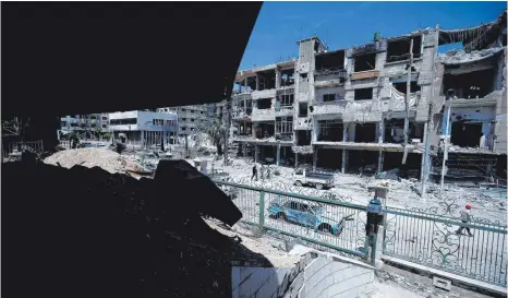  ?? FOTO: DPA ?? Nach dem Inferno: Menschen gehen mehr als eine Woche nach dem mutmaßlich­en Giftangrif­f an zerstörten Häusern und Autos im syrischen Duma vorbei.