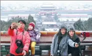  ?? WANG ZHUANGFEI / CHINA DAILY ?? Tourists and residents take photos atop Jingshan Mountain against the backdrop of the snow-covered Palace Museum in Beijing on Tuesday. Snow fell in many provinces and temperatur­es plunged in many areas by more than 8 C as winter showed it isn’t over...