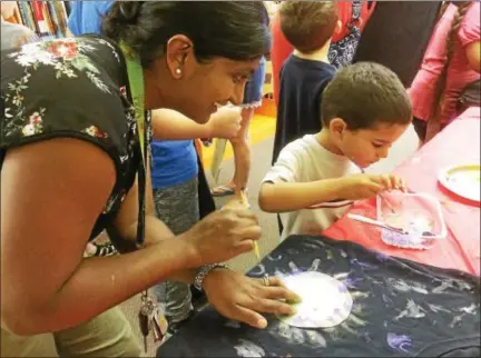  ?? EVAN BRANDT — DIGITAL FIRST MEDIA ?? Trappe resident Geraldine Petr and her son Jerome, 3, paint an eclipse on his shirt during a program Monday at the Pottstown Regional Public Library, which ended with the giveaway of eclipse glasses.