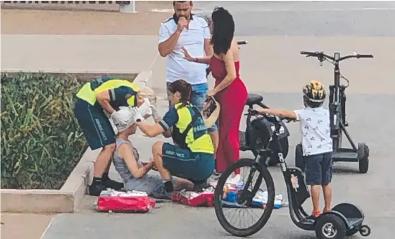  ??  ?? A woman bleeding from the head is tended by paramedics after crashing her hire bike in Surfers Paradise on Sunday at the corner of View Avenue and the Esplanade.