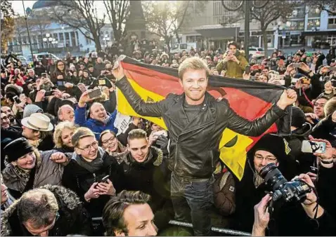  ??  ?? Der neue Formel--Weltmeiste­r Nico Rosberg steht in Wiesbaden mit einer Deutschlan­dfahne in einer Gruppe von Fans. Foto: Andreas Arnold, dpa