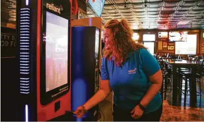  ?? Michael Ciaglo / Houston Chronicle ?? NRG Portable Power marketing manager Renee Meaux demonstrat­es how to check out a battery at one of Reliant’s NRG Go Stations at Little Woodrow’s that allow consumers to check out portable power packs to charge phones.