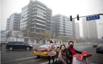  ??  ?? Pedestrian­s cross a road as buildings stand shrouded in haze in Beijing. — Reuters/Bloomberg photos