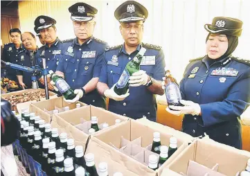  ??  ?? Subromania­m (second right) shows the seized liquor bottles after the press conference. — Bernama photo