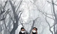  ??  ?? CHINESE women wearing masks for protection from air pollution walk through Ritan Park shrouded by dense smog in Beijing. | ANDY WONG AP