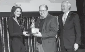  ??  ?? Jim Rice of the Little Rock Convention and Visitors Bureau receives the Tourism Person of the Year award from Miss Arkansas Savannah Skidmore while Gov. Asa Hutchinson looks on.