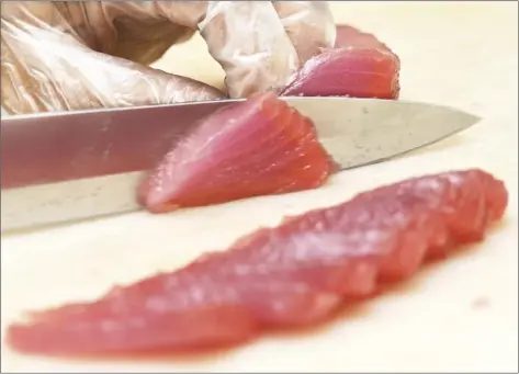  ?? The Maui News / MATTHEW THAYER photo ?? Takamiya Market Meat Department Supervisor Margie Domingo slides a very sharp knife across a piece of ahi Wednesday.