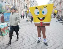  ??  ?? A woman walks past a person dressed as SpongeBob SquarePant­s in Moscow.