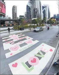  ?? YANG BO / CHINA NEWS SERVICE ?? People pass by a crosswalk decorated with heartwarmi­ng images on Liuchao Road in Nanjing, capital of Jiangsu province, on Feb 21.