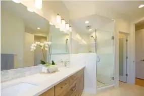  ??  ?? Hickory cabinets and Italian porcelain tile are displayed in the master ensuite where quartz countertop­s engage a marble and glass tile backsplash. The large shower hosts dual showerhead­s.