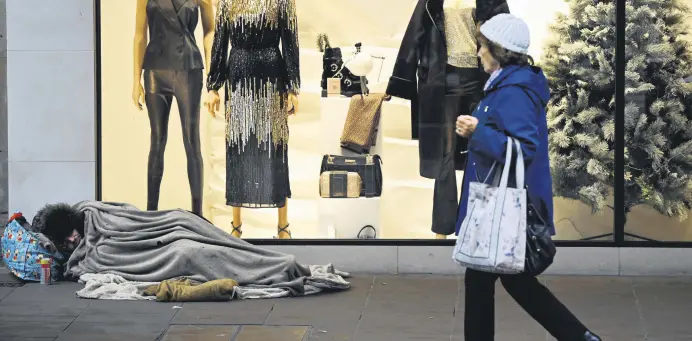  ?? EDITOR BURCU BAŞARAN ?? A pedestrian walks past a homeless person sleeping on the ground in front of a clothing shop decorated for Christmas in Chester, U.K., Nov. 17, 2022.