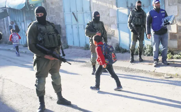  ??  ?? Palestinia­n children walk past Israeli soldiers on their way to school in the West Bank city of Hebron, Feb. 12, 2019.