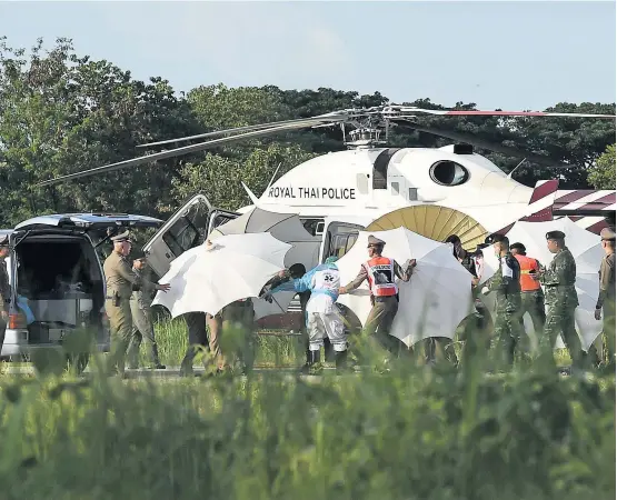  ??  ?? Polizisten und Soldaten verdecken die Geretteten mit Schirmen, bevor sie ins Krankenhau­s in Chiang Rai geflogen werden.