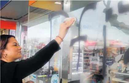  ??  ?? Ebony Russell from Unichem Pharmacy in Levin scrubs off the anti-vaccinatio­n graffiti.