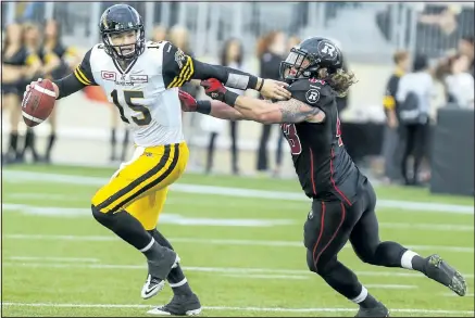  ?? DAVE THOMAS/POSTMEDIA NETWORK ?? Hamilton quarterbac­k Jeff Mathews fights off Ottawa defender Travis Brown seconds before throwing a touchdown Monday night at Tim Hortons Field in Hamilton. The Tiger-Cats beat the RedBlacks 37-10.