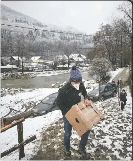 ?? (AP/Andreea Alexandru) ?? Nicolae carries a box containing basic food, hygiene and medical products on a muddy slope in Nucsoara, Romania.