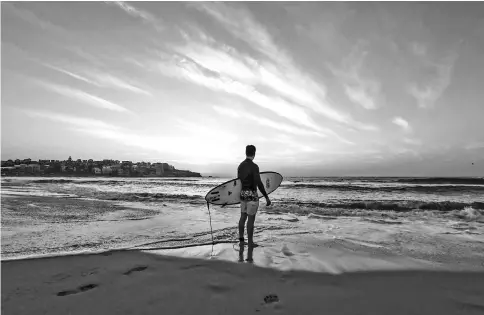  ??  ?? A surfer stands at the water’s edge with his surfboard during sunrise at Bondi Beach in Sydney, Australia, on Jan 23. — WP-Bloomberg photo