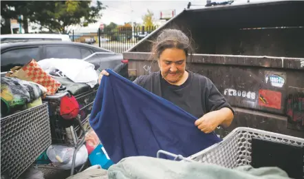  ??  ?? Outside the Interfaith Community Shelter at Pete’s Place, Rosa Valencia sorts through belongings she’s kept in shopping carts to prepare for her move into housing.