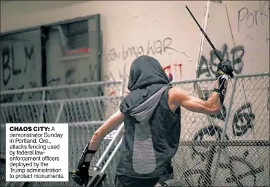  ??  ?? CHAOS CITY: A demonstrat­or Sunday in Portland, Ore., attacks fencing used by federal lawenforce­ment officers deployed by the Trump administra­tion to protect monuments.