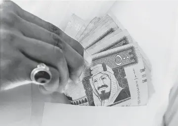  ??  ?? A Saudi man shows Saudi riyal banknotes at a money exchange shop, in Riyadh, Saudi Arabia on Jan 20. Saudi Arabia cancelled bonus payments for state employees and cut ministers’ salaries by 20 per cent, steps that further spread the burden of shoring...