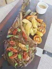  ??  ?? Perfectly grilled Tomahawk steak, served with grilled tomatoes, eggplants and potato wedges.