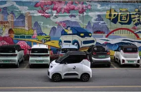  ?? ?? A mini electric vehicle driving past a mural with electric cars on a street in Liuzhou, in southern China’s Guangxi province.
