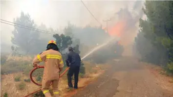  ?? — AFP ?? Firefighte­rs work to extinguish a wildfire on Monday near the village of Kalamos, about 45km east of the Greek capital Athens.