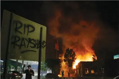  ?? The Associated Press ?? HARSH SPOTLIGHT: “RIP Rayshard” is spray-painted on a sign as flames engulf a Wendy’s restaurant on June 13 during protests in Atlanta. The restaurant was where Rayshard Brooks was shot and killed by police the previous evening following a struggle in the restaurant’s drive-thru line. The deadly police shooting soon after the city erupted in fiery demonstrat­ions protesting police brutality have cast a harsh spotlight on cracks in Atlanta’s reputation for Black prosperity in politics and business.