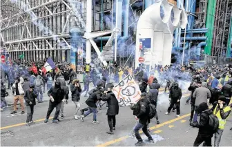  ?? Michel Euler / Associated Press ?? Demonstrat­ors run away from tear gas fired by police during a protest in Paris against pension reform plans. The strikes have disrupted transport across France and beyond.