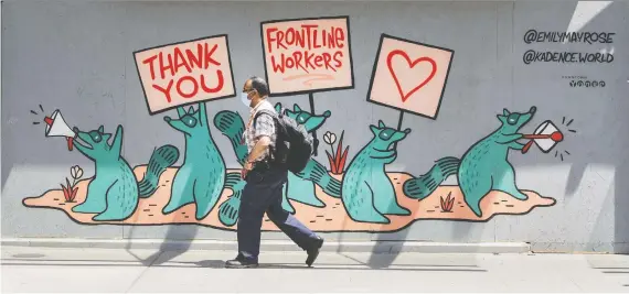  ?? PETER J. THOMPSON ?? A pedestrian wearing a mask walks past a mural supporting frontline workers on Toronto’s Yonge Street during the COVID-19 pandemic earlier this week. Almost every sector of the Canadian economy has been hit hard by the shutdown, with those relying on consumer spending suffering the most.