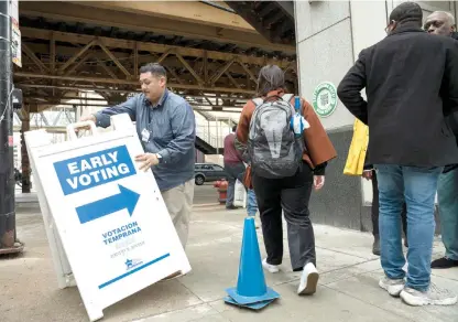  ?? PAT NABONG/SUN-TIMES ?? Mario Garcia sets up a sign outside the Loop supersite on the first day of early voting for the primary election.