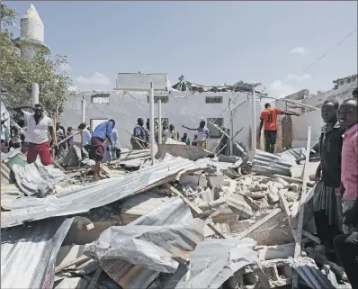  ??  ?? Somalis search for bodies amidst wreckage at the scene of the blast outside the compound of a district headquarte­rs.