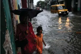  ?? (AP Photo/Ramon Espinosa) ?? Children walk through their neighborho­od street flooded by heavy rains, in Havana, Cuba, Friday, June 3, 2022. Heavy rains have drenched Cuba with almost non-stop rain for the last 24 hours as tropical storm watches were posted Thursday for Florida, Cuba and the Bahamas as the system that battered Mexico moves to the east.