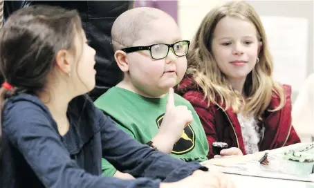  ?? NICK BRANCACCIO ?? Huntre Allard, centre, sits with classmates Bella Peralta, left, and Josie Lombardo on Monday while handing out John Deere-themed cupcakes at Our Lady of Perpetual Help Catholic Elementary School. It was Huntre’s first day back in class after brain surgery.