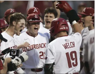  ?? (NWA Democrat-Gazette/Charlie Kaijo) ?? Arkansas’ Charlie Welch (19) is greeted by teammates outside the dugout after his three-run home run with two outs in the eighth inning during Monday night’s series-clinching victory over Nebraska in the NCAA Fayettevil­le Regional. The Razorbacks now face North Carolina State in the super regionals this weekend.