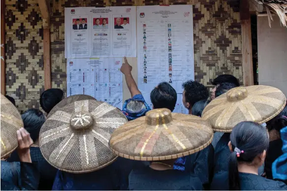  ?? AFP ?? Indonesian voters read a list of candidates before casting their ballots at a polling station in Lebak, Banten province, yesterday