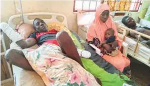  ?? ?? Mr Yahaya Muhammed Galadima, lying on his sick bed. Beside him is his wife, Fatima, and their baby Photo: Umar Muhammed